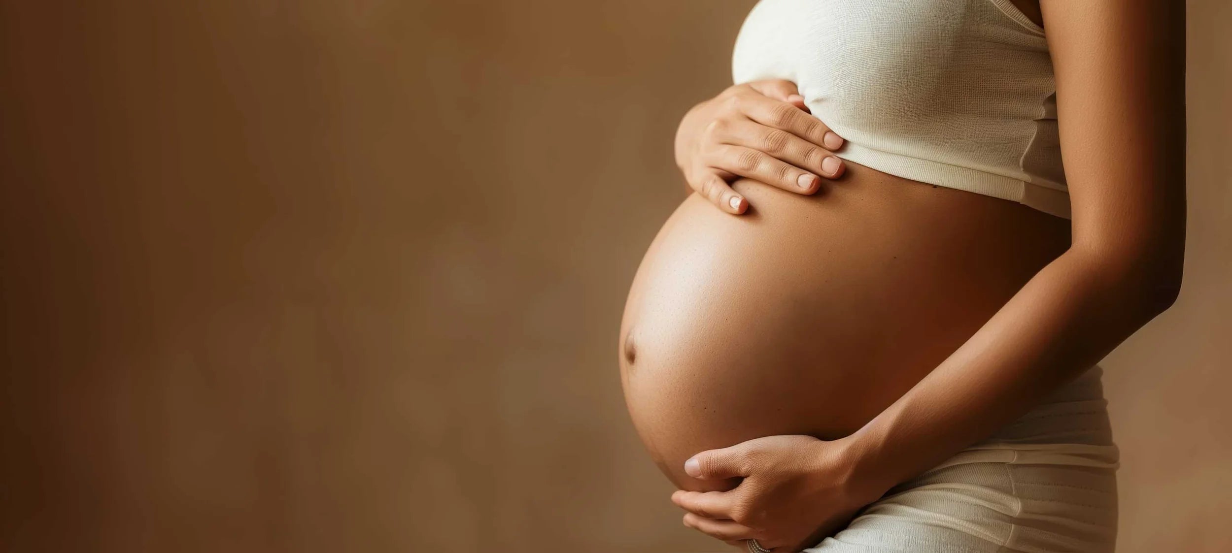 Pregnant person holding their belly against a brown background